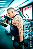 Фото мужчины с татуировкой сбоку во время силового упражнения с гантелями