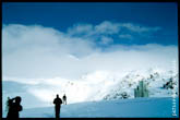 Фото фигур на фоне снежных склонов. Впереди - вершины Эльбруса, справа - памятник героям обороны Приэльбрусья