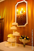 Фото свадебного торта на столе, рядом свадебный букет, свечи на стене