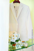 Фото букета невесты из белых цветов и бутоньерки жениха с белой розой на фоне белого мужского костюма
