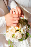 Фото рук жениха и невесты с обручальными кольцами на фоне букета невесты из белых роз