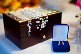 Фото обручальных колец в синей бархатной коробочке, вдали - деревянная шкатулка невесты с украшениями