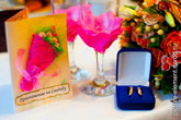 Открытка-приглашение на свадьбу, свадебные бокалы с цветками, коробочка с обручальными кольцами на столе