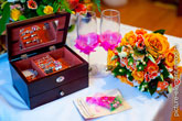 Фото открытой деревянной шкатулки с украшениями невесты, золотые кольца сверху на открытке, свадебные бокалы и букет невесты