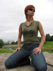 Фото девушки в джинсах, зеленой майке и солнечных очках, сидящей на коленях