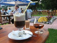 Фото бокалов с коктейлем и коньяком на столе в летнем кафе, вдали люди